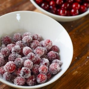 A white bowl of sugar coated cranberries next to a bowl of plain cranberries.