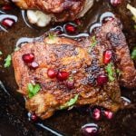 Close up of the crispy skin on pan seared chicken thighs. They are garnished with pomegranate arils.