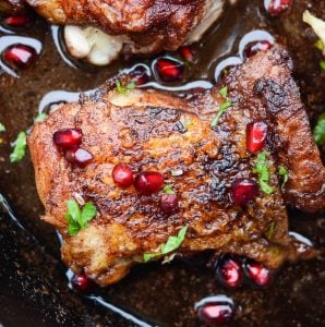 Close up of the crispy skin on pan seared chicken thighs. They are garnished with pomegranate arils.