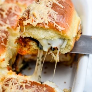 a pesto chicken parmesan slider being removed from the pan with a spatula