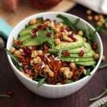 White bowl of salad next to cutting board with pomegranate and sweet potato