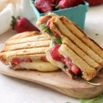 Two halves of a panini on cutting board by basket of strawberries