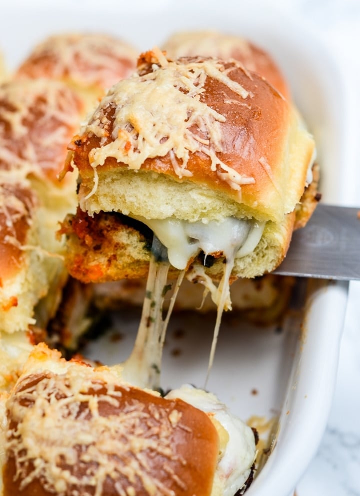 a single Pesto Chicken Parmesan Slider being pulled from the pan with cheese stringing from it