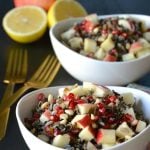 Two white bowls of rice salad next to silverware and cut lemons