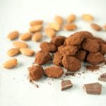 pile of chocolate covered almonds next to raw almonds