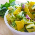 white bowl of mango avocado salsa next to fresh cilantro