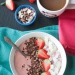 white smoothie bowl on blue napkin by cup of coffee and toppings