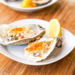 Two halved oysters on a w white plate with lemon wedge