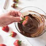 Hand dipping fresh strawberry into chocolate