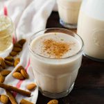 clear glass of horchata with almonds, cinnamon and towel next to it