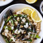 A bowl of pasta with asparagus garnish with lemon wedges.