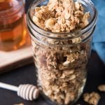 A mason jar of granola next to jar of honey and honey dipper