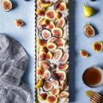 One long tart next to cut pieces of fresh figs and a gray napkin