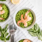 Three bowls of couscous and prawns on a striped napkin next to silverware and spinach