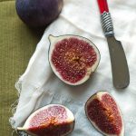 Cut figs on a white napkin next to cheese knife