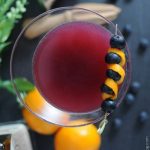 martini glass with blueberry and orange peel garnish
