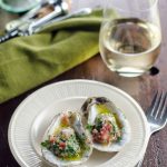 Two oysters on a white plate next to green napkin and white wine