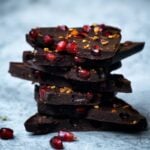 a stack of broken pieces of winter raw chocolate bar next to pomegranate arils