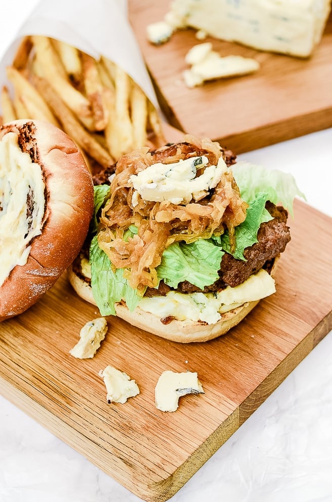 roasted garlic burger on a cutting board with a wedge of cambozola and fresh french fries behind it.