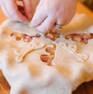 two hands placing pie crust decorations on a pie