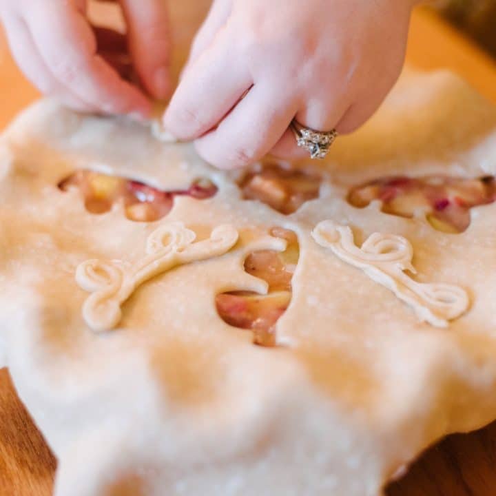 two hands placing pie crust decorations on a pie