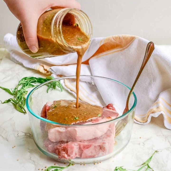 A hand pouring marinade from a mason jar onto pork chops in a bowl.