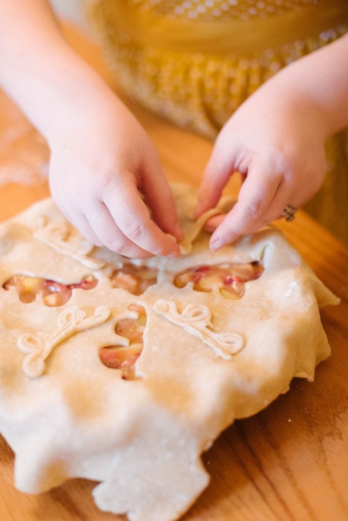 two hands decorating the top crust of a pie