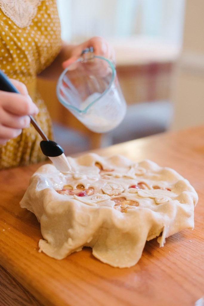 cream being brushed onto the top crust of a pie