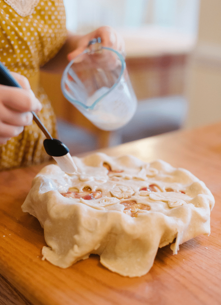 hands brushing an egg wash on top of raw pie crust