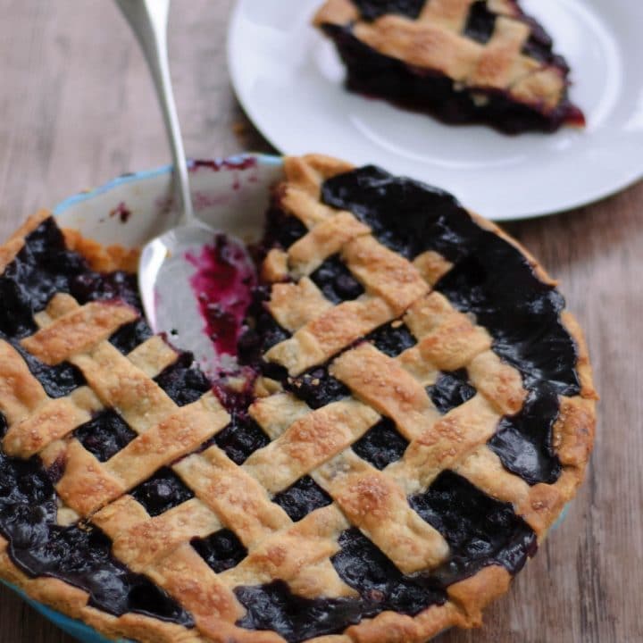 Spiced blueberry pie with a slice cut out next to a plate with the slice on it.