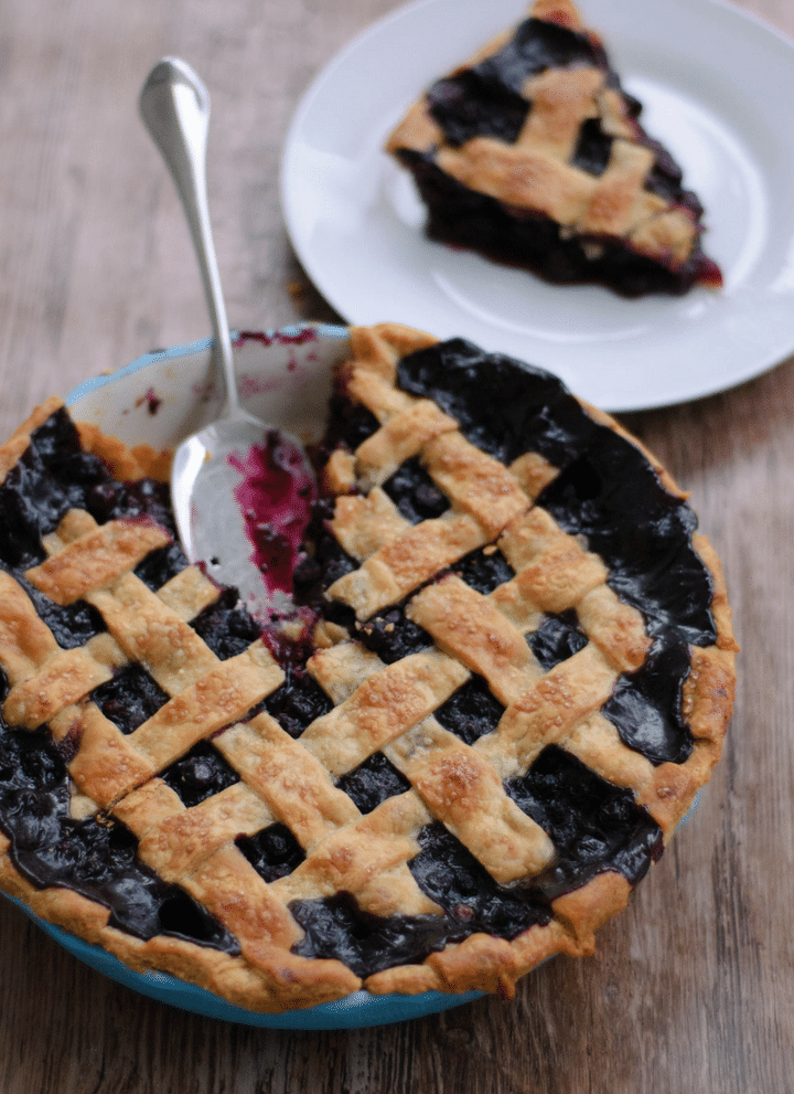 Spiced blueberry pie missing one piece. The piece is on a white plate in background