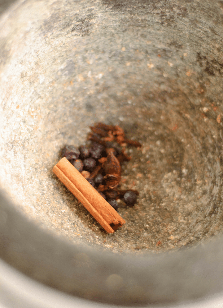A cinnamon stick and fresh spices inside of a mortar and pestle.
