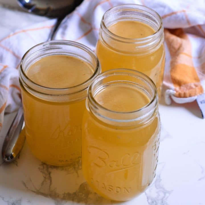 three mason jars of homemade turkey stock next to a towel and ladle