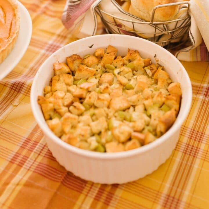 A white bowl of brown butter cornbread dressing on an autumnal tablecloth