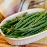 A small serving dish of haricots verts on an autumnal tablecloth.