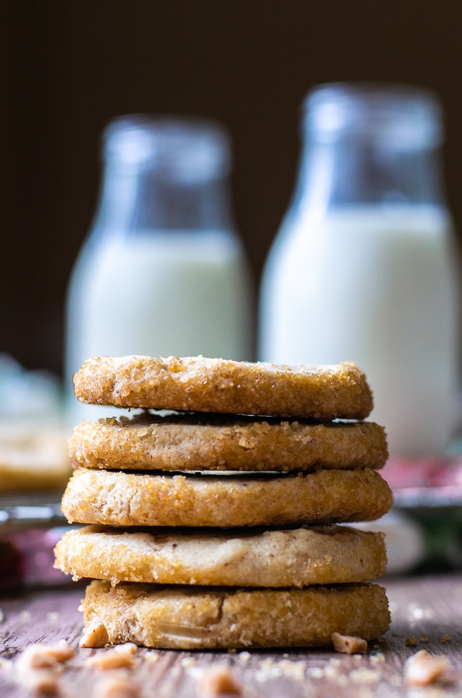 Five round shortbread cookies stacked in front of two jars of milk