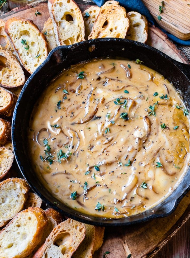 Overhead image of baguette slices surrounding a cast iron pan of caramelized onion dip