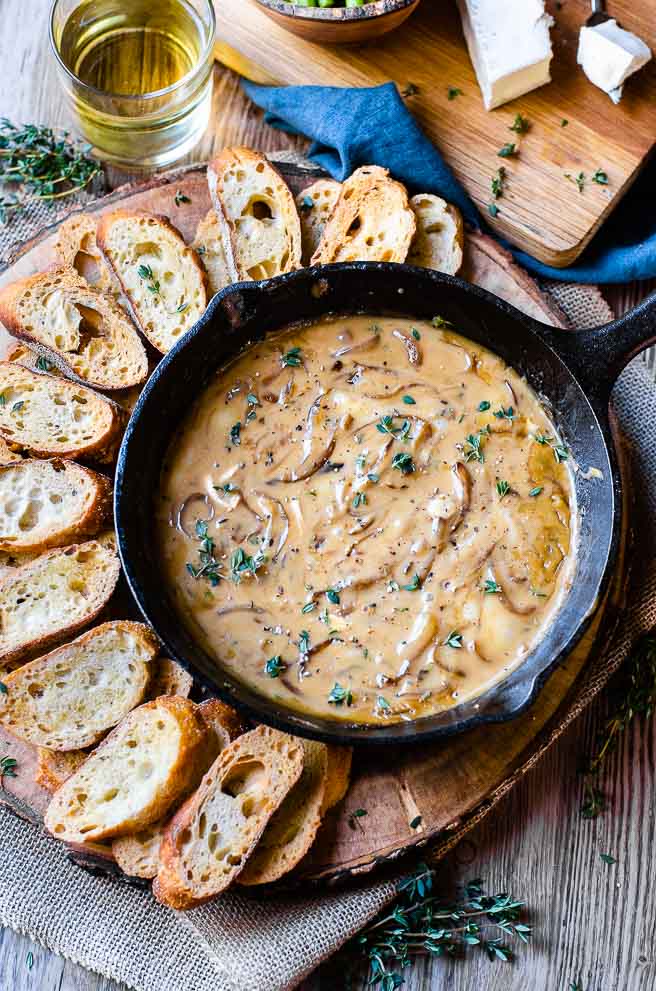 overhead image of a cast iron pan of hot caramelized onion dip on a wooden board surrounded by baguette slices