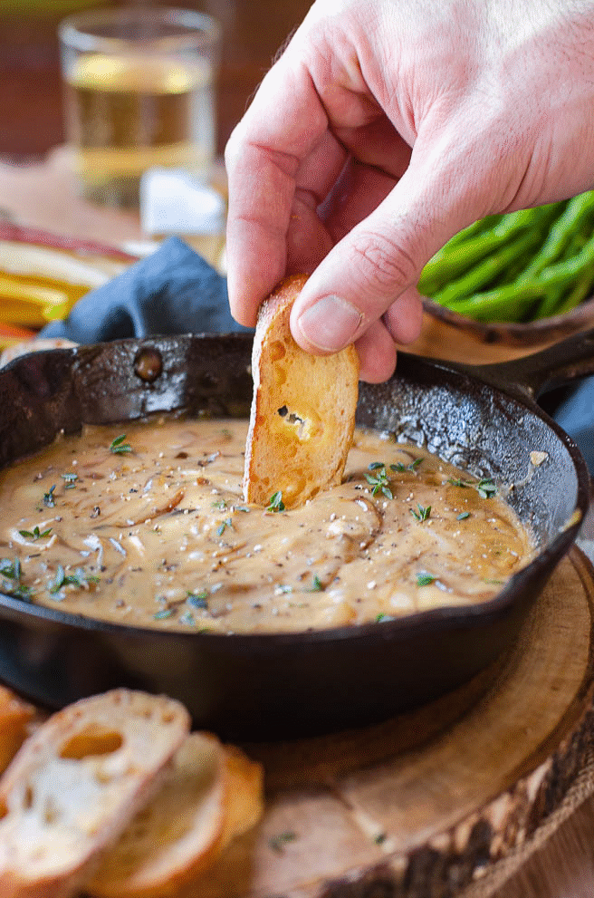 Gif showing a piece of baguette being dipped into hot caramelized onion dip