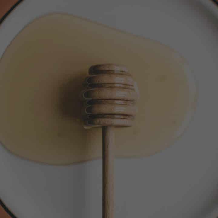 Black overlay on a picture of a honeycomb dipper on a plate with honey spread out.