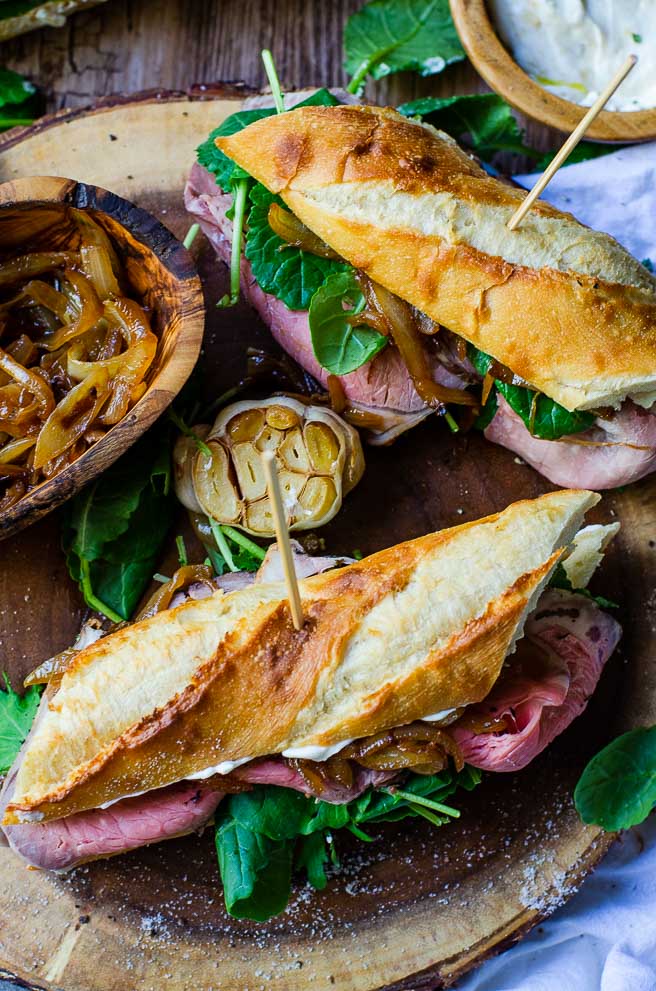 overhead image of two assembled leftover prime rib sandwiches next to a bowl of caramelized onions and roasted garlic