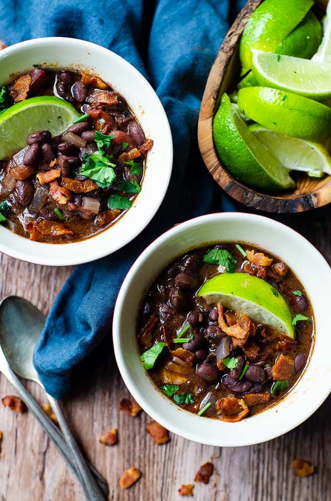 An overhead image of two bowls of black bean soup next to a wooden bowl of limes