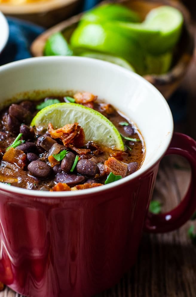 Close up of black bean soup garnished with a lime in a red bowl