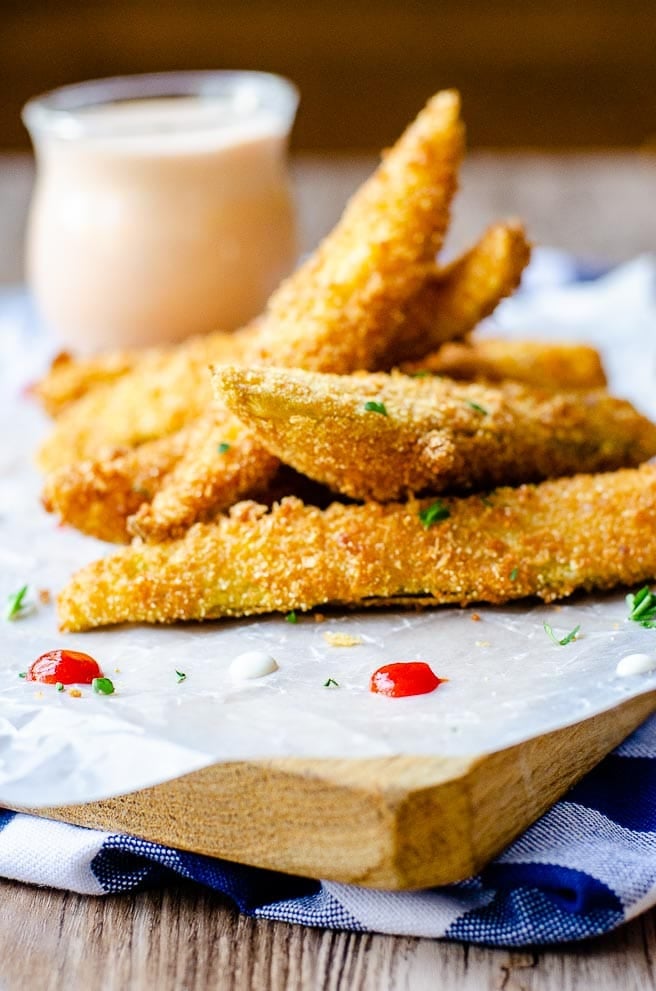 direct view of a pile of fried pickles on a wooden board and dipping sauce in the background