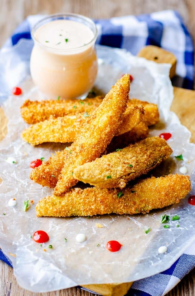 Seven friend pickles in front of a clear container of dipping sauce