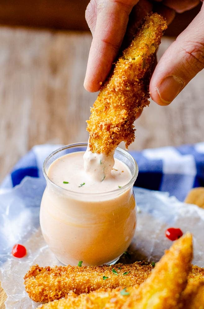 A hand dipping a deep fried pickle into sriracha ranch dipping sauce