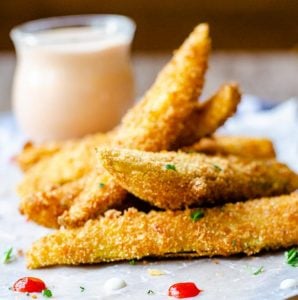 close up of deep fried pickle spears with a clear jar of sriracha ranch being them