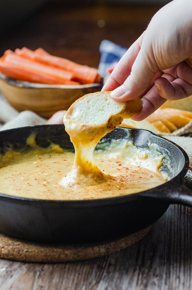 hands dipping a piece of bread into beer cheese dip