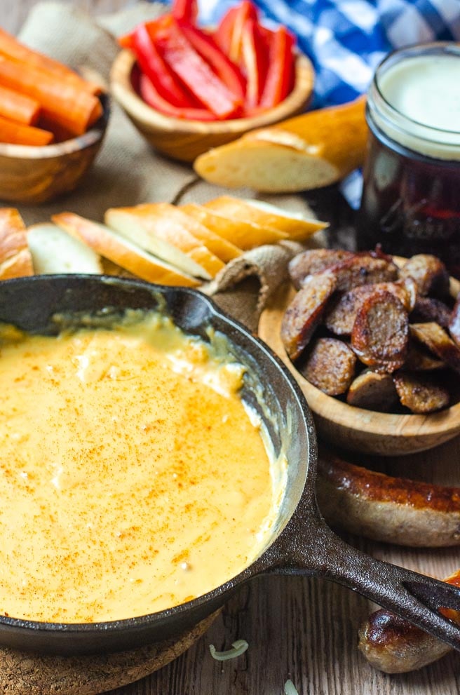 Cast iron pan of beer cheese dip surrounded by bowls of things to dip in it