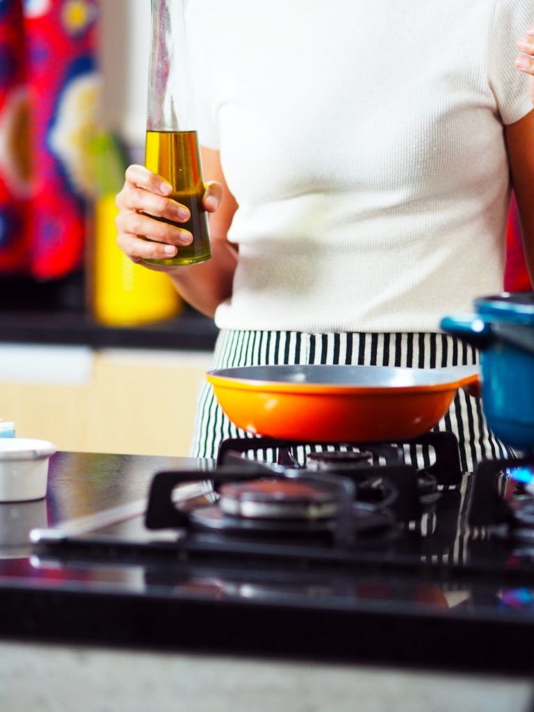 Woman holding a cruet of oil above a pan